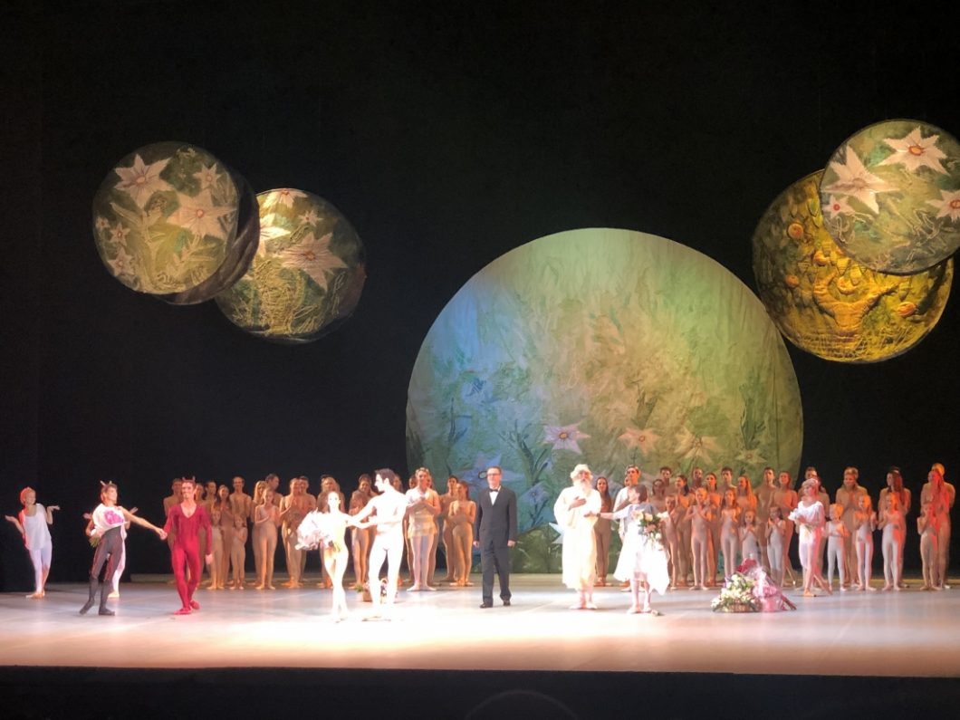 Performers fill the stage during a ballet performance. The set features large orbs representing the mood and planets.