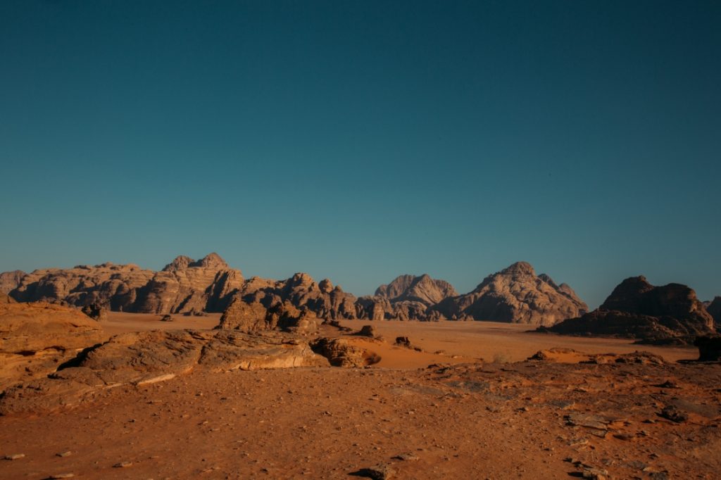 The Wadi Rum desert landscape, filled with ranges of rocky mountains and rust-colored sand valleys under a crystal clear blue sky.