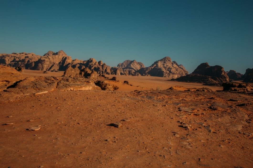 The Wadi Rum desert in Jordan, a vast and sandy desert landscape with brown and red sand and rocky hills and a clear blue sky overhead.