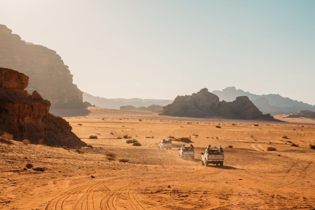 Three white Jeeps head out into the Wadi Rum desert for a Wadi Rum jeep tour on a bright and hazy day.