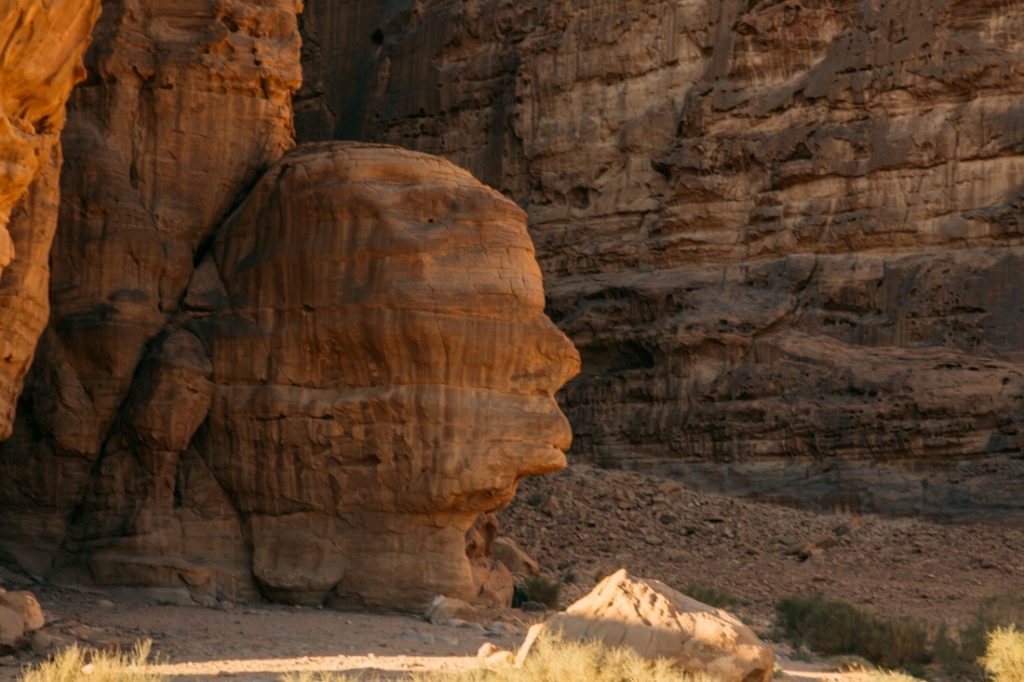 A unique rock formation in the Wadi Rum desert resembles the facial profile of a human. The ancient rock has layers of colors, and is shaded from the sun.
