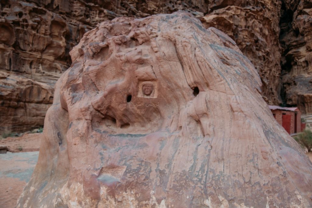 A large boulder rock formation has ancient carvings cut into the side, detailing histories from thousands of years ago.