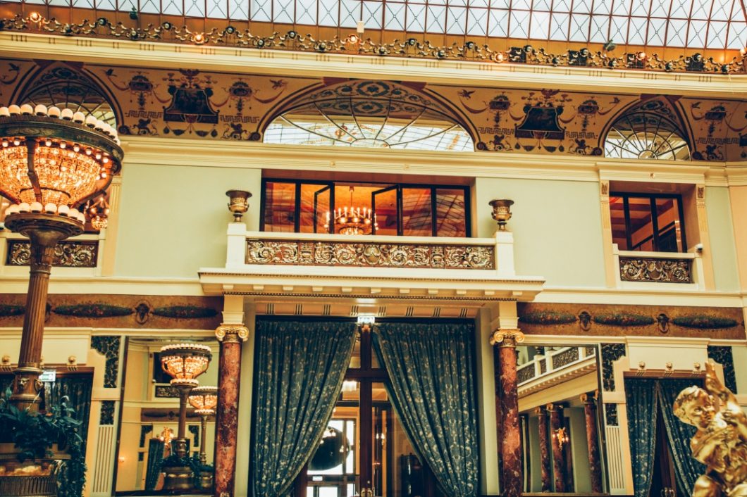 A photo looking up to a balcony inside the Piazza grand dining room inside the Metropol Hotel. The balcony features large glass doors and overlooks the entire dining room.