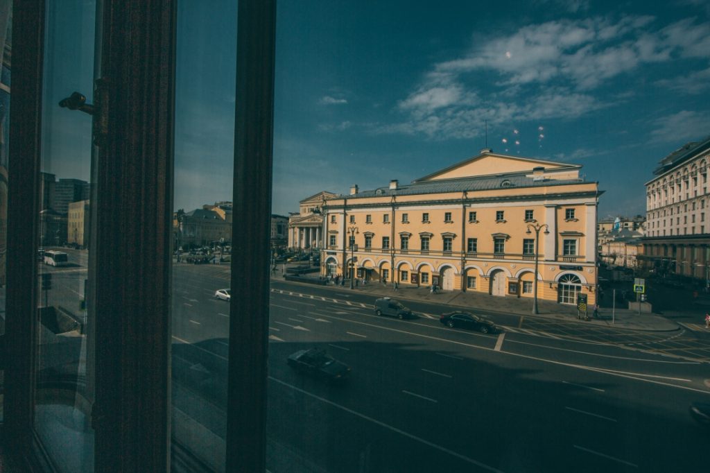 A view of the Bolshoi Theater from a room inside the Metropol Hotel. The view looks out onto a city street on a clear, cloudless day.