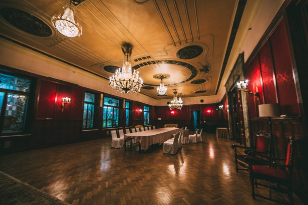 A large private dining room inside the Metropol Hotel. The room has parquet wood floors and tall ceilings with chandeliers handing down, and a long banquet table in the center.