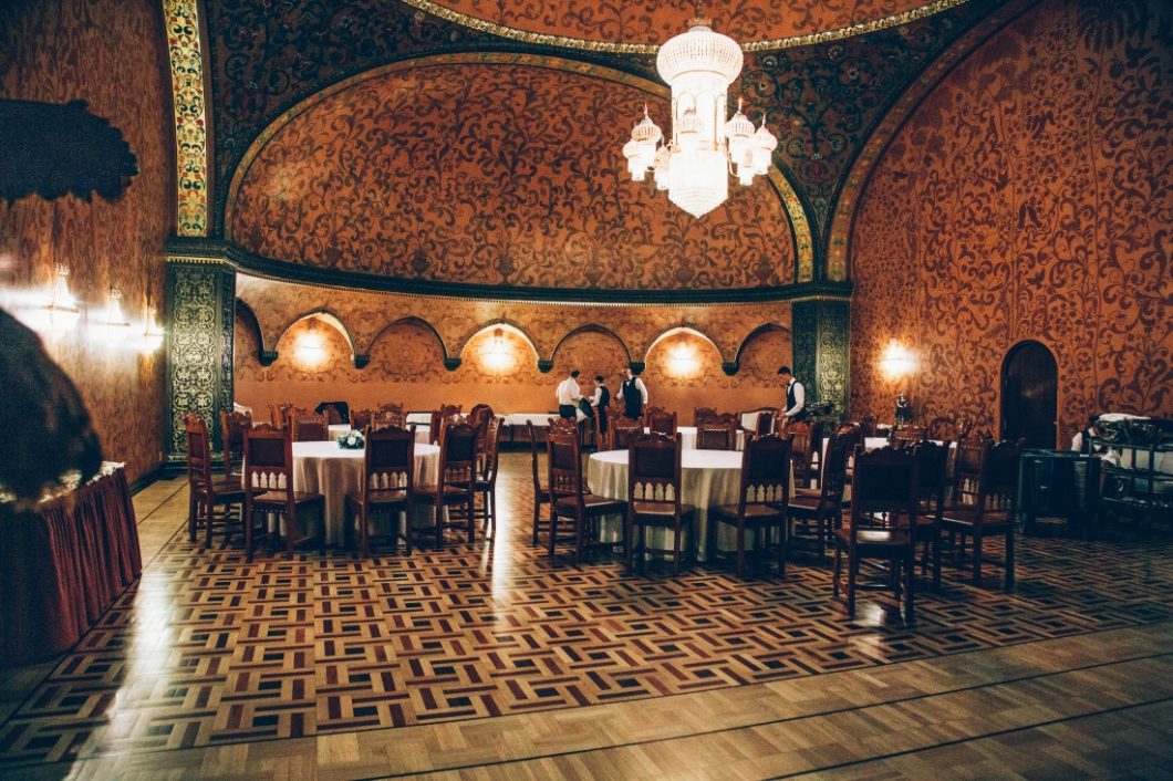 A dimly lit dining room features several dining tables on a parquet wood floor. This room is written as "The Boyarsky" in the Metropol Hotel-based novel, A Gentleman in Moscow.