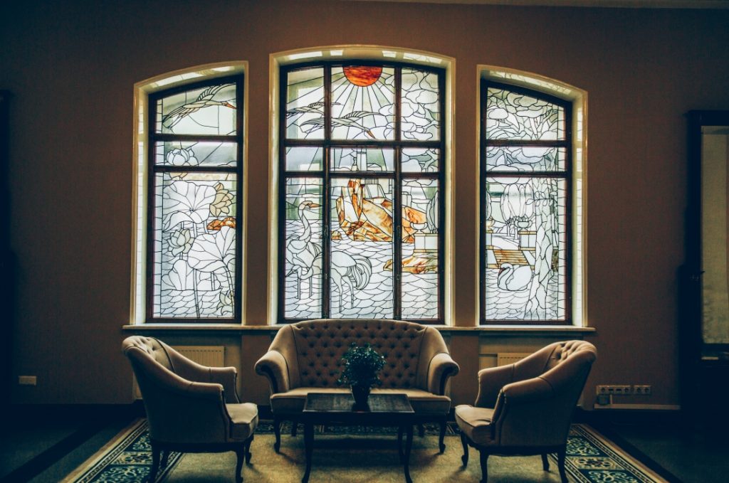 A quaint seating area features four upholstered chairs in front of a three panel stained glass window.