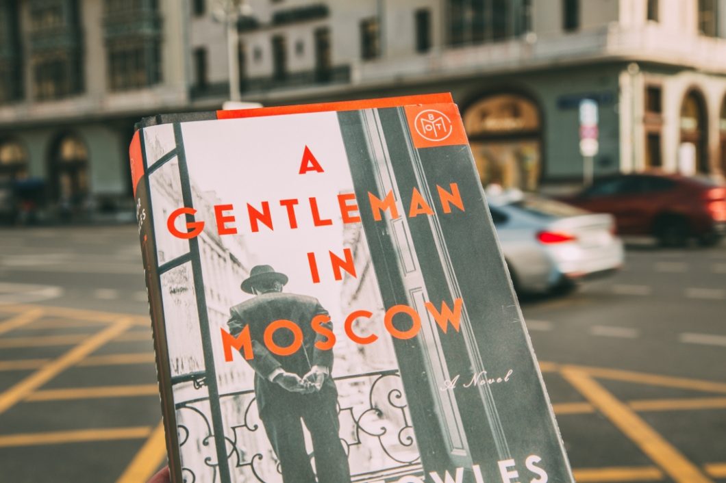 The book cover of A Gentleman in Moscow, held up in front of a Moscow street.