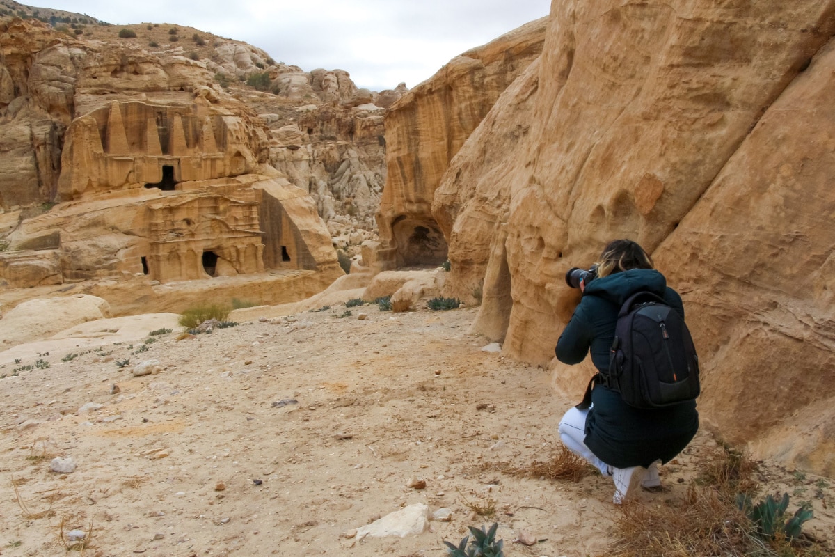 Woman in black jacket photographs the Obelisk tomb in ancient Petra city in Jordan. The building is carved out of sandstone right into the rock. Theme of travel in Jordan.