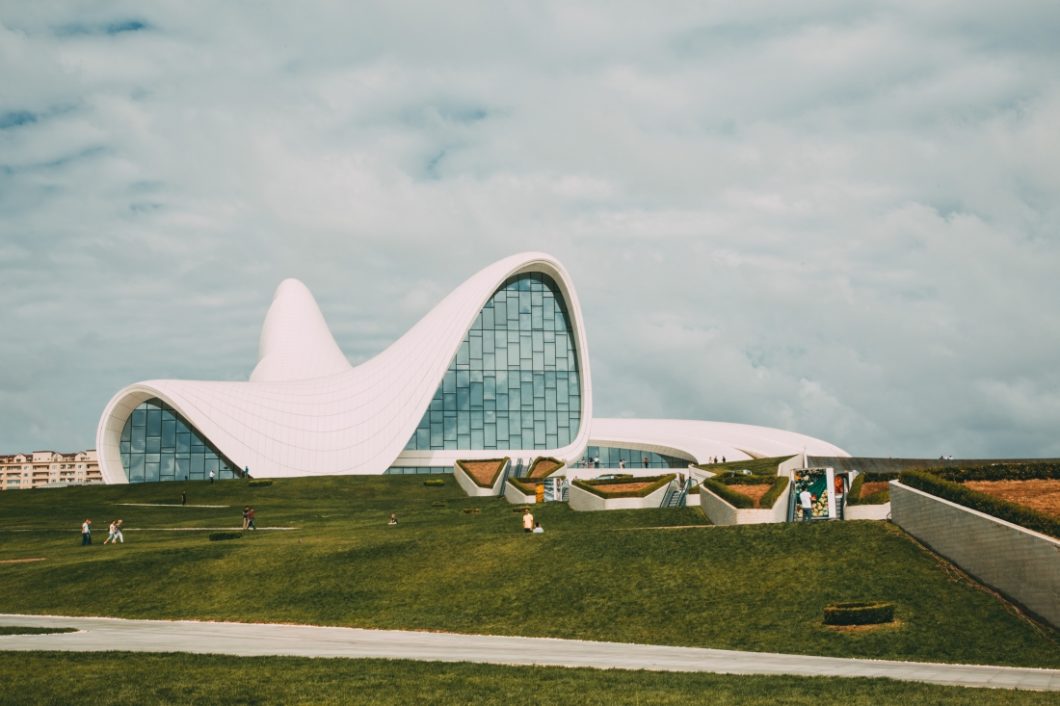 A long-distance exterior shot of the Heydar Aliyev Center in Baku, Azerbaijan against a cloudy blue sky.