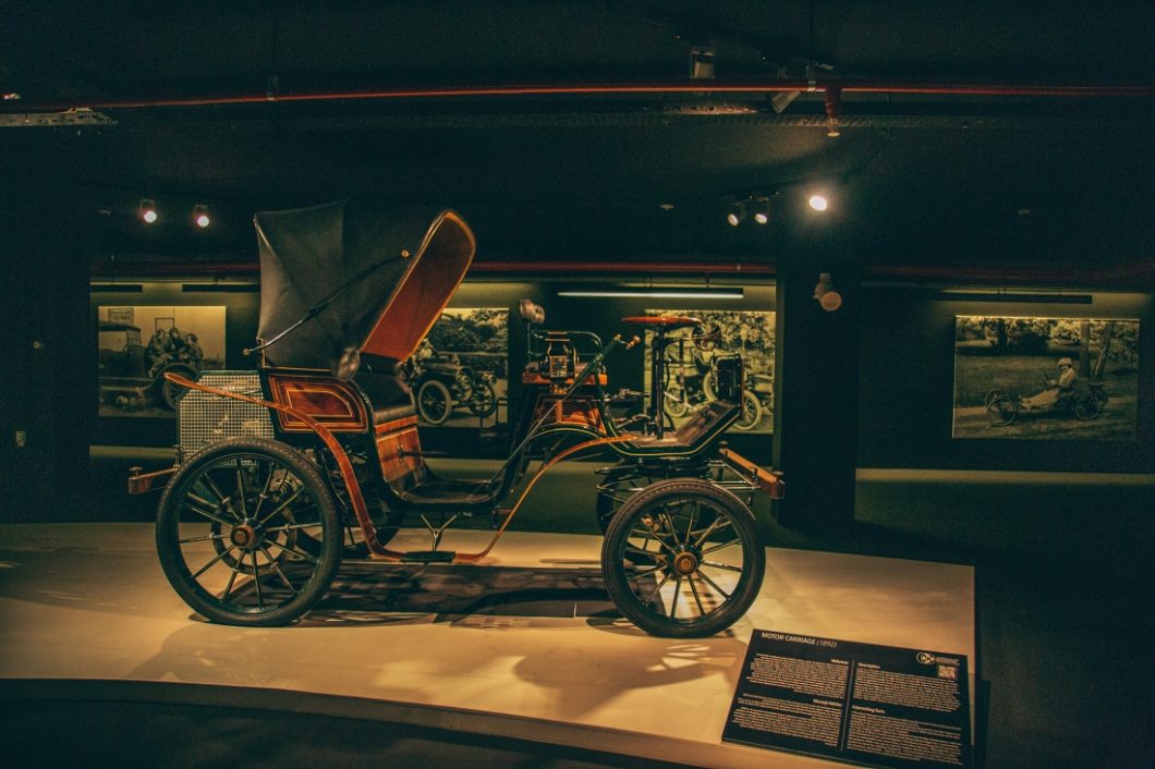 A Daimler Motor Carriage, dated back to 1892, on display at the Heydar Aliyev Center’s Classic Car Exhibit in Baku, Azerbaijan. This old car has a carriage-style body, awing over the bench seats where the riders sat, and a raised bench seat in front for the driver.