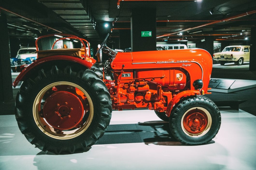 A red 73 Porsche Diesel Tractor with large back wheels on display at the Heydar Aliyev Center's Classic Car Exhibit in Baku, Azerbaijan.