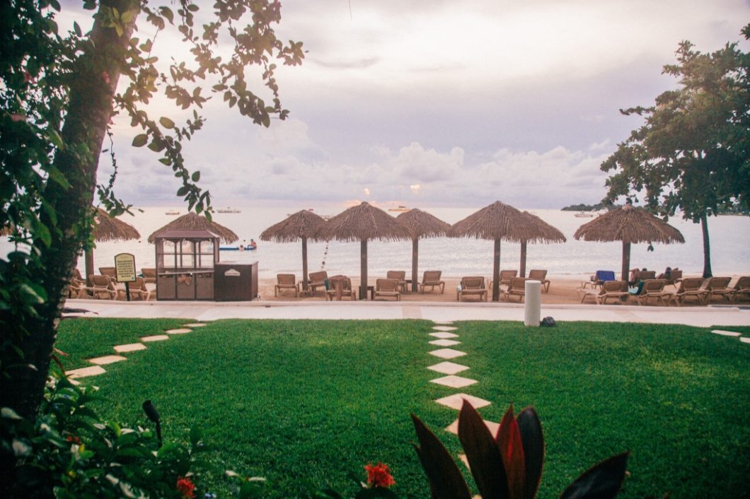 The view from a resort room porch at Sandals Negril. The oceanfront views show a small lawn, then a sandy beach with cabanas, umbrellas, and lounge chairs.