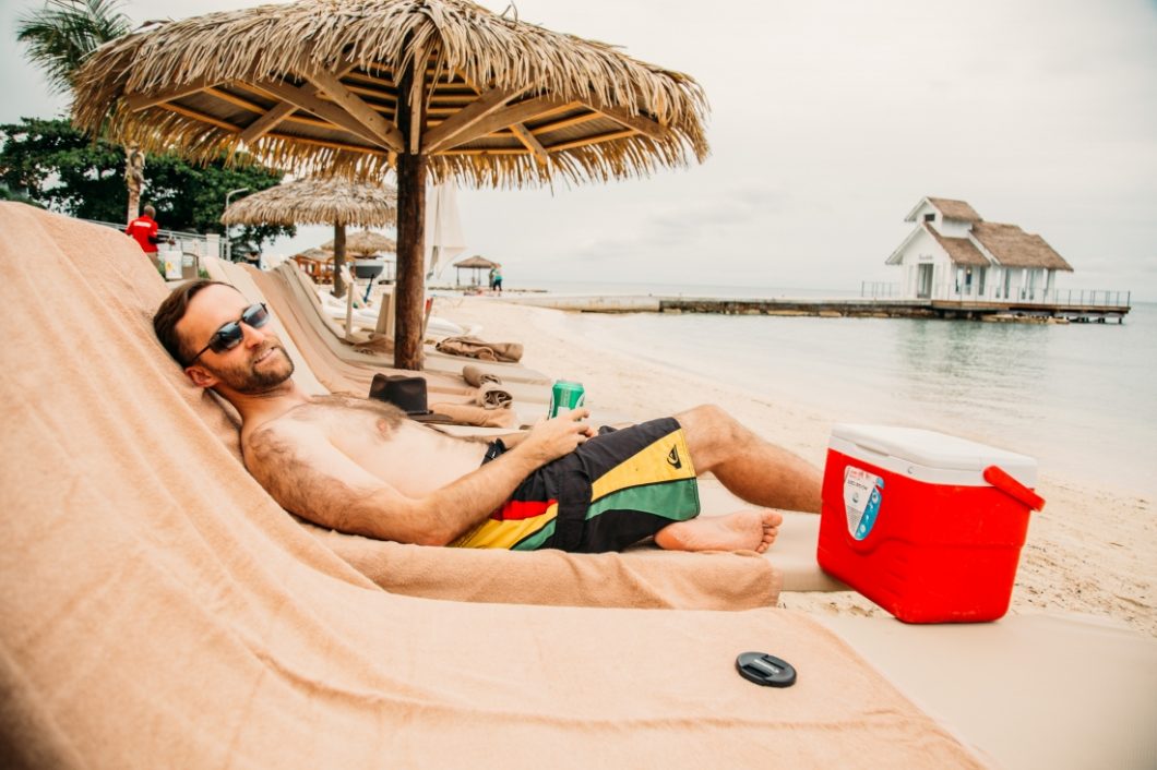 Zac lounging on a beach chair holding an NA beer and smiling.