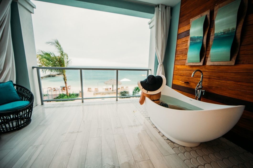 Lindsey wearing an oversized black and white sunhat, lounging in a soaking tub on the balcony of her Sandals Montego Bay room