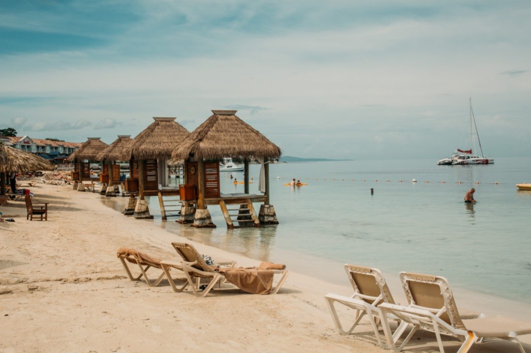 Overwater huts and lounge chairs line the sandy beach of the Sandals Montego Bay Resort