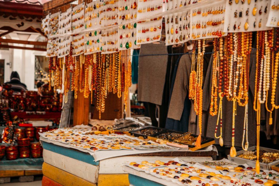 A street display of amber jewelry at a street market. Earrings, necklaces, and pendants are displayed hanging from metal hangers.