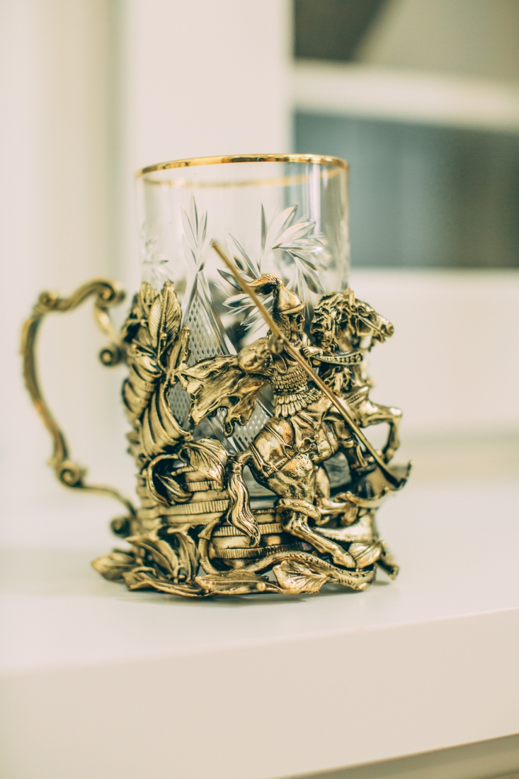 A gold-rimmed glass sits in an ornate gold glass holder with a scene of an ancient Russian solder on a horse.