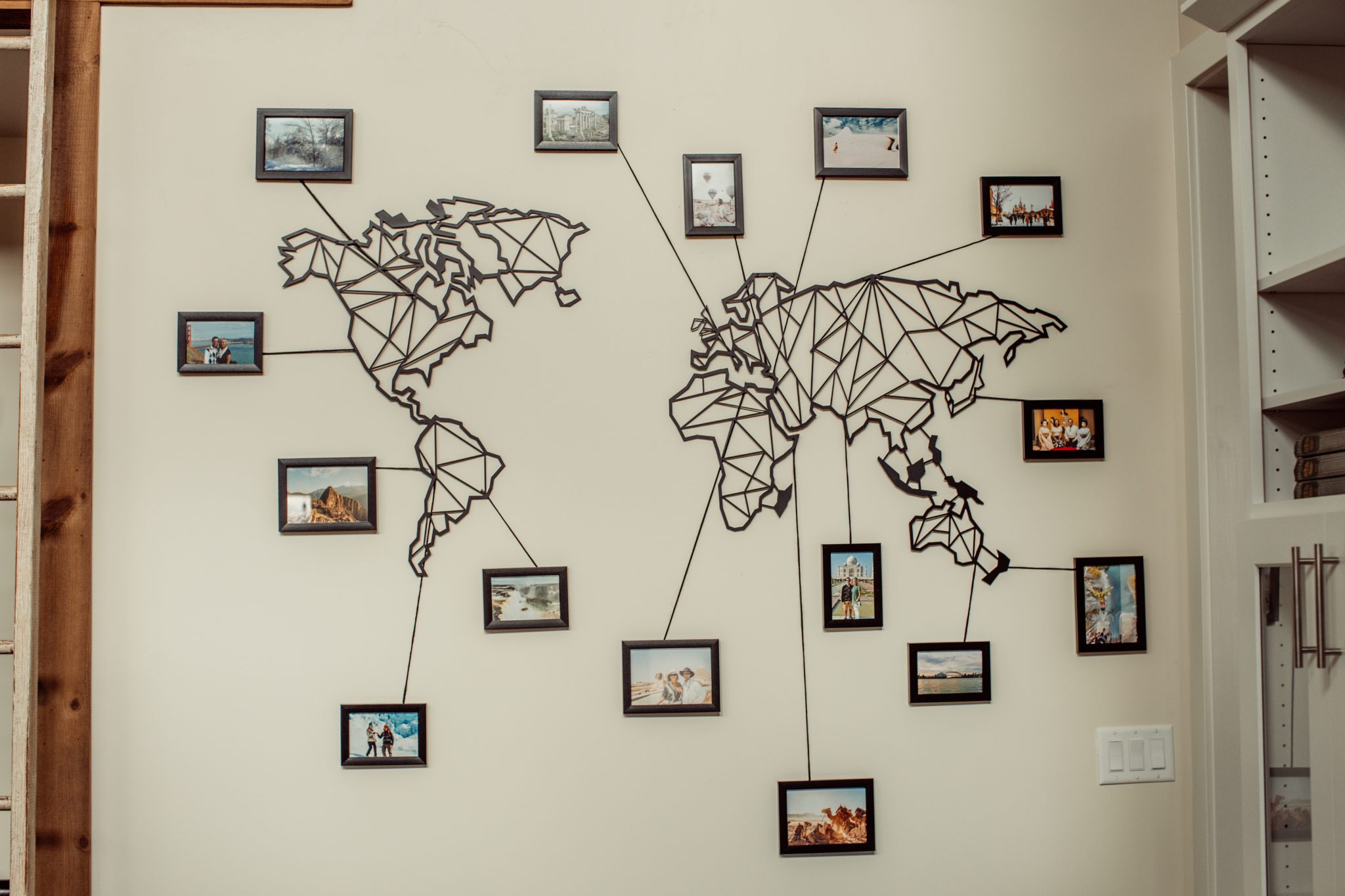 This creative travel wall features a laser-cut world map made from metal with framed pictures surrounding it. Each photo is tied to a location with a strand of yarn, showing where the photo was taken.