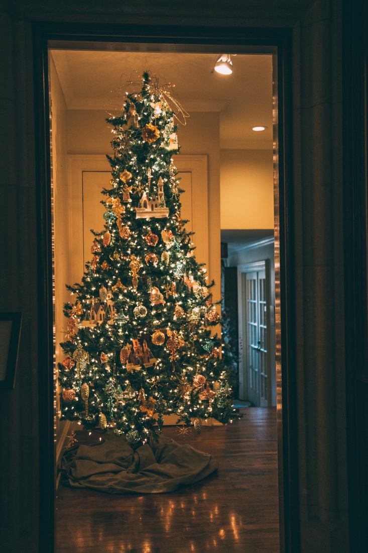 A tall Christmas tree framed in a doorway, lit with lights and large, decorative ornaments.