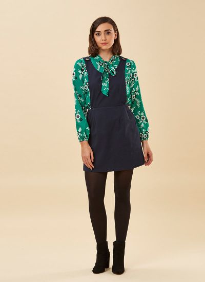 A model wears a Navy Pinafore dress over a green patterned long-sleeve blouse from Modcloth alternative clothing store Jeanie Clothing. 