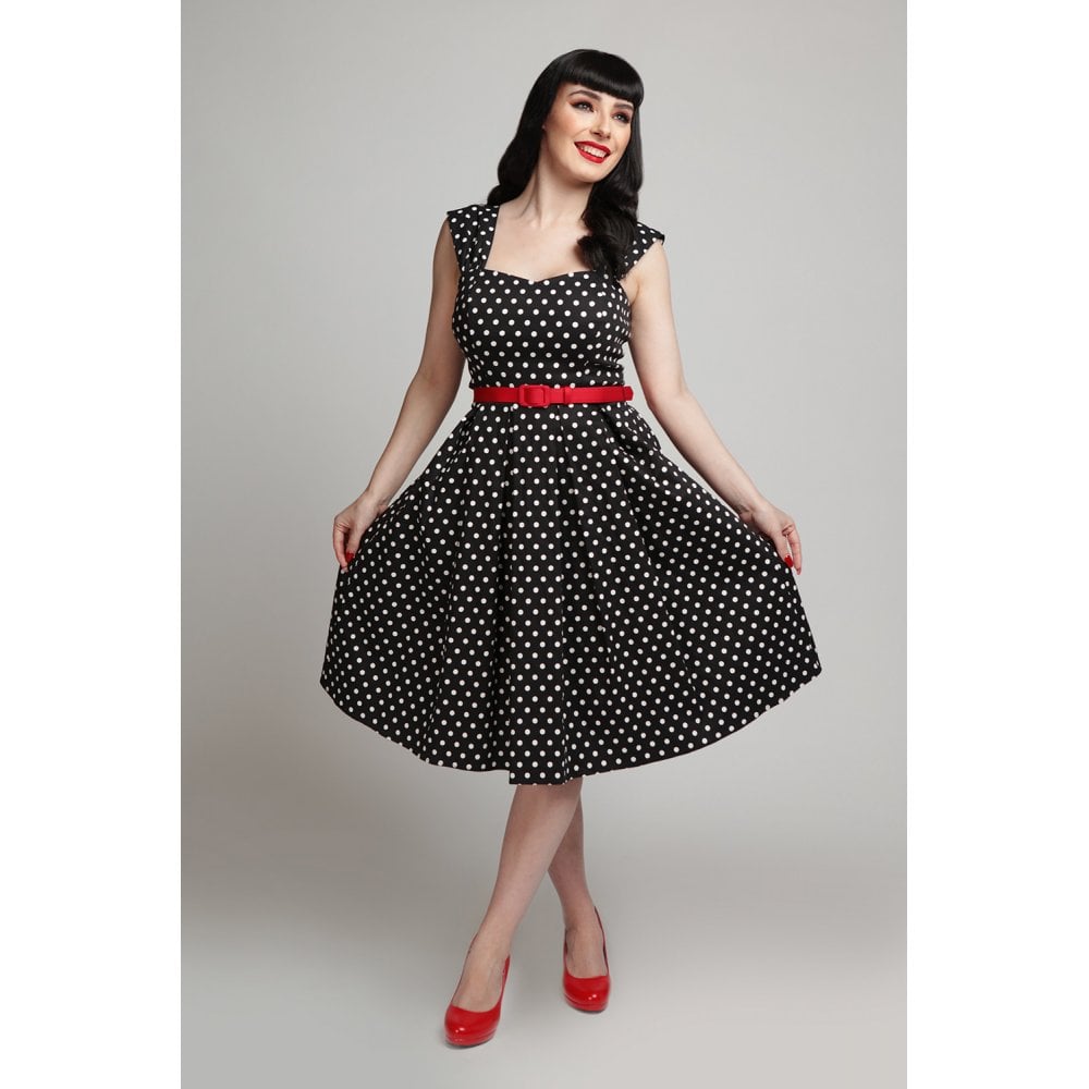 A model wears a vintage style black and white polka dot dress, accessorized with a skinny red belt and red high heels.