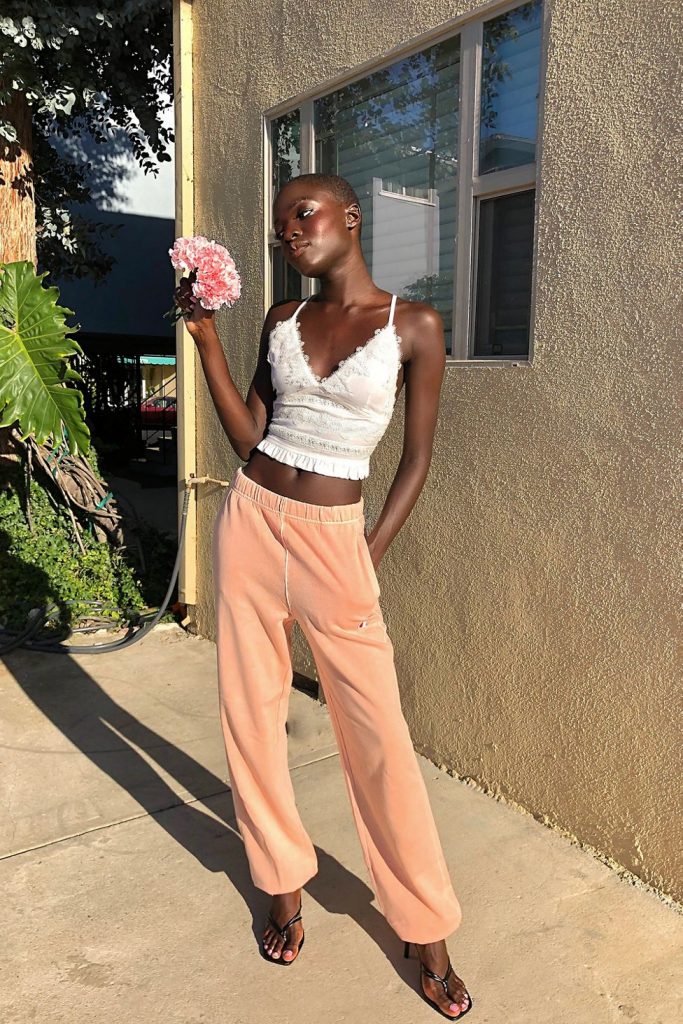 A woman wearing a white cropped tank top with Champion Vintage Wash Oversized Sweatpants, holding pink flowers