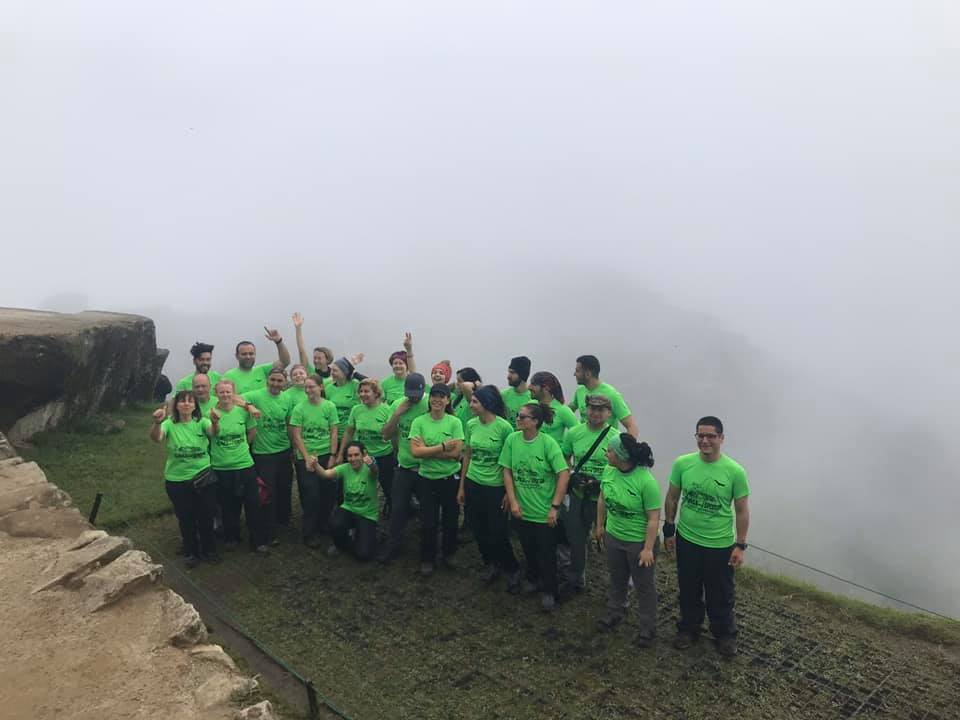 A tour group gathers for a photo in at an overlook point for Machu Picchu, but the village and mountains are obscured by dense fog.
