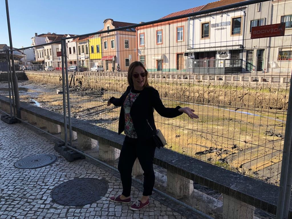 A woman stands on the street, posing in front of The Aveiro in Portugal, emptied of water, showing a muddy riverbed. 