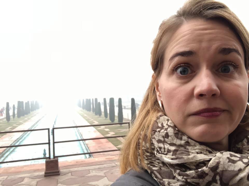 A woman takes a selfie in front of the courtyard of the Taj Mahal, but the giant palace is obscured completely by a thick fog.