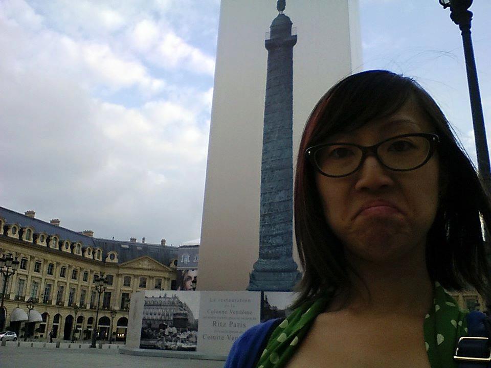 A woman poses in front of the Place Vendôme in Paris, France, which is covered completely in construction scaffolding.