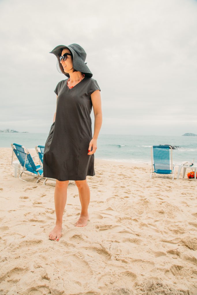 Lindsey walking on the beach wearing a black SCOTTeVEST dress and black sun hat