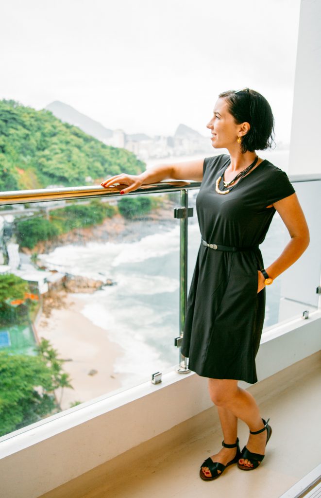 Lindsey standing on a resort balcony wearing a black dress that is belted at the waist