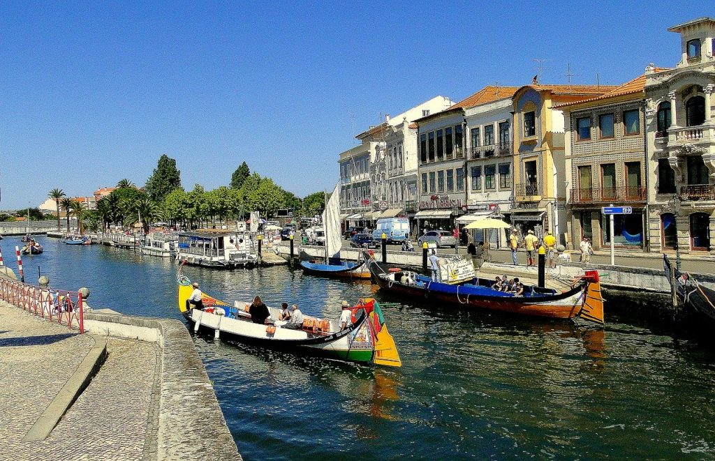 The river of Aveiro in Portugal on a clear summer day, filled with gondolas and tourists on boat rides.