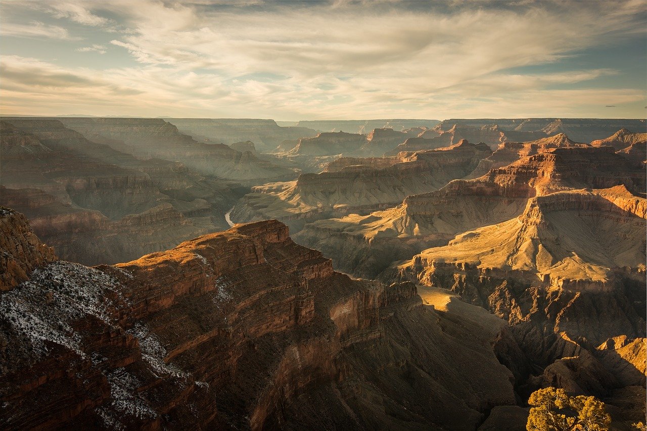 A professional image of the Grand Canyon at golden hour. The sun sets over the expansive canyon, casting sunbursts over the mountaintops.