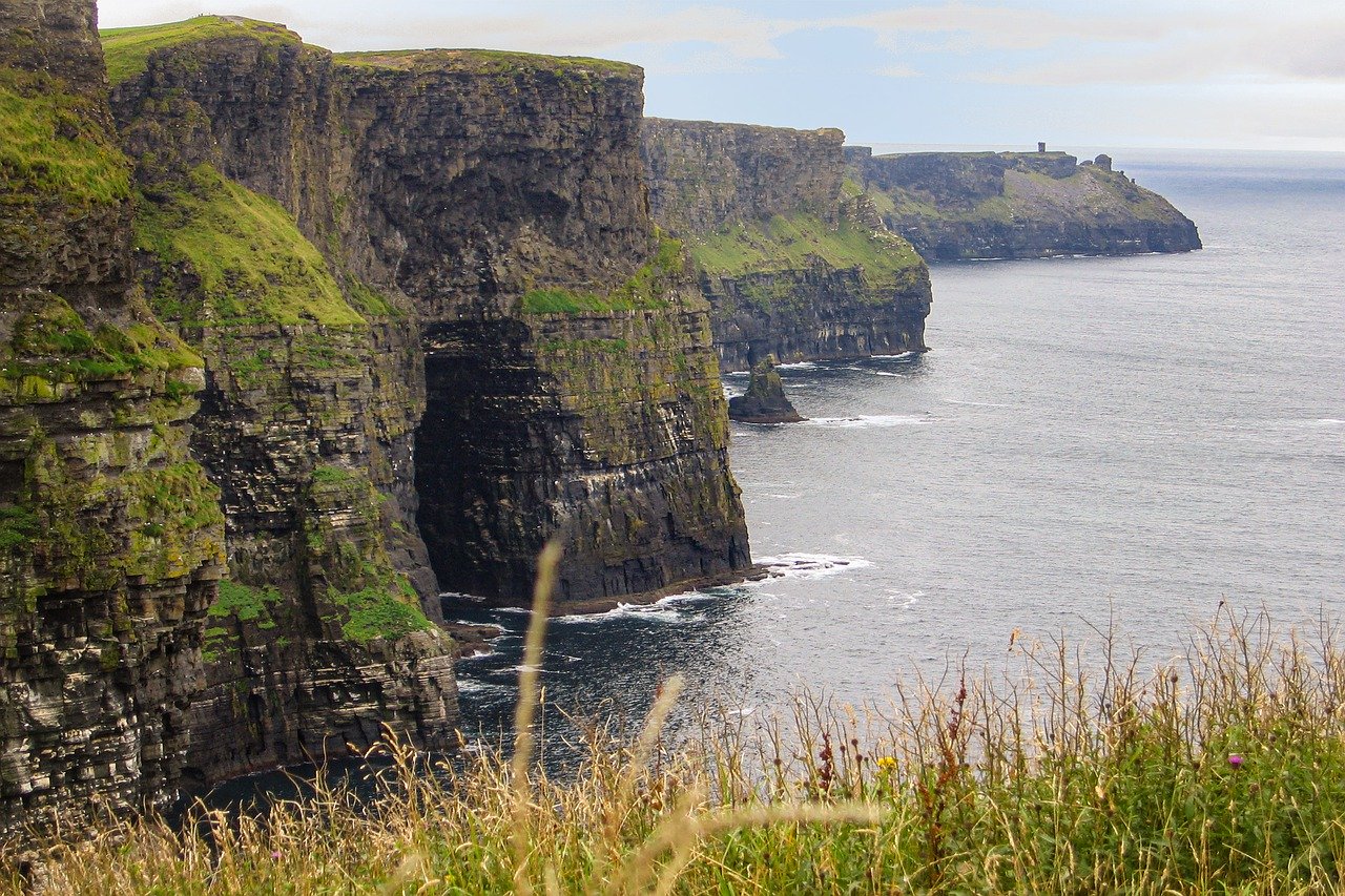 A professional photo of the Cliffs of Moher in Ireland with clear skies and a panoramic view of the cliffs down the shoreline for miles.