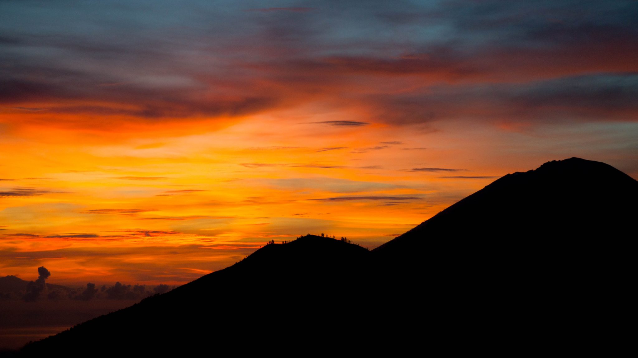 The silhouette of Mount Batur in Bali, Indonesia against a deep orange sunset.