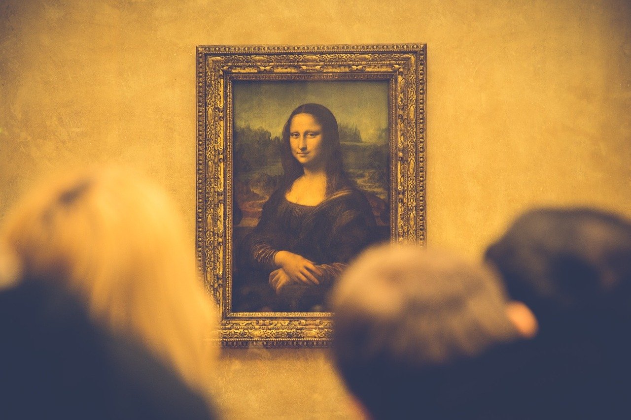 A professional image of the Mona Lisa. The photo is zoomed in, making the painting look large and close, and is filtered to have a yellowish hue. The tops of visitors' heads are visible, but the painting is in focus.