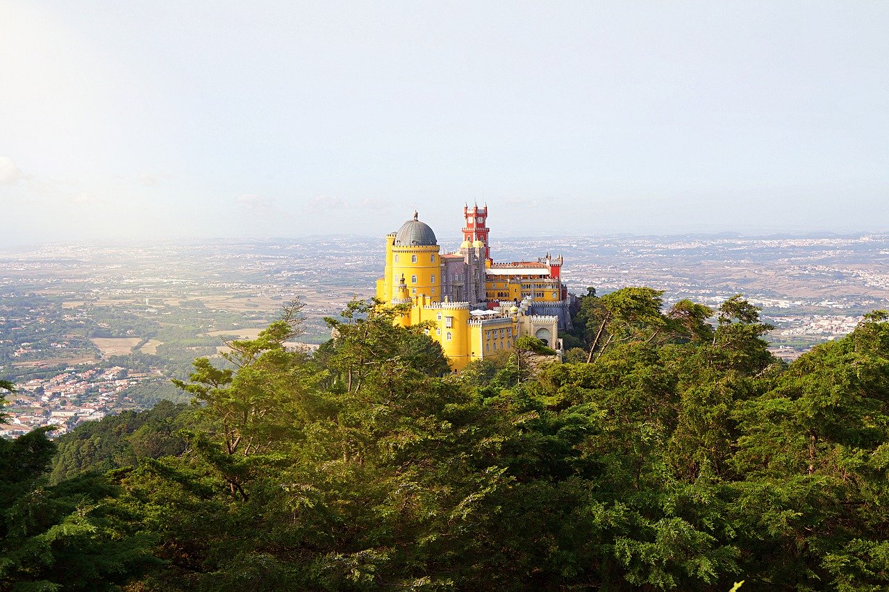 A professional photo of Sintra, Portugal, with the giant castle on the lush green hill overlooking a panoramic of the city. It's a sunny day and the view goes on for miles.