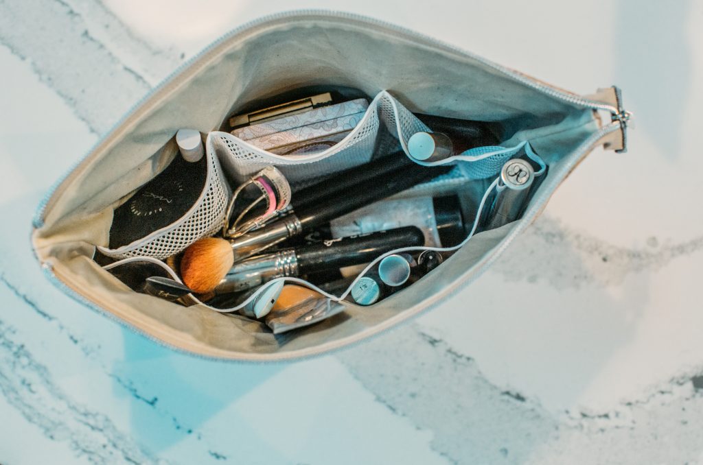 A makeup bag filled with cosmetics on a marble countertop.