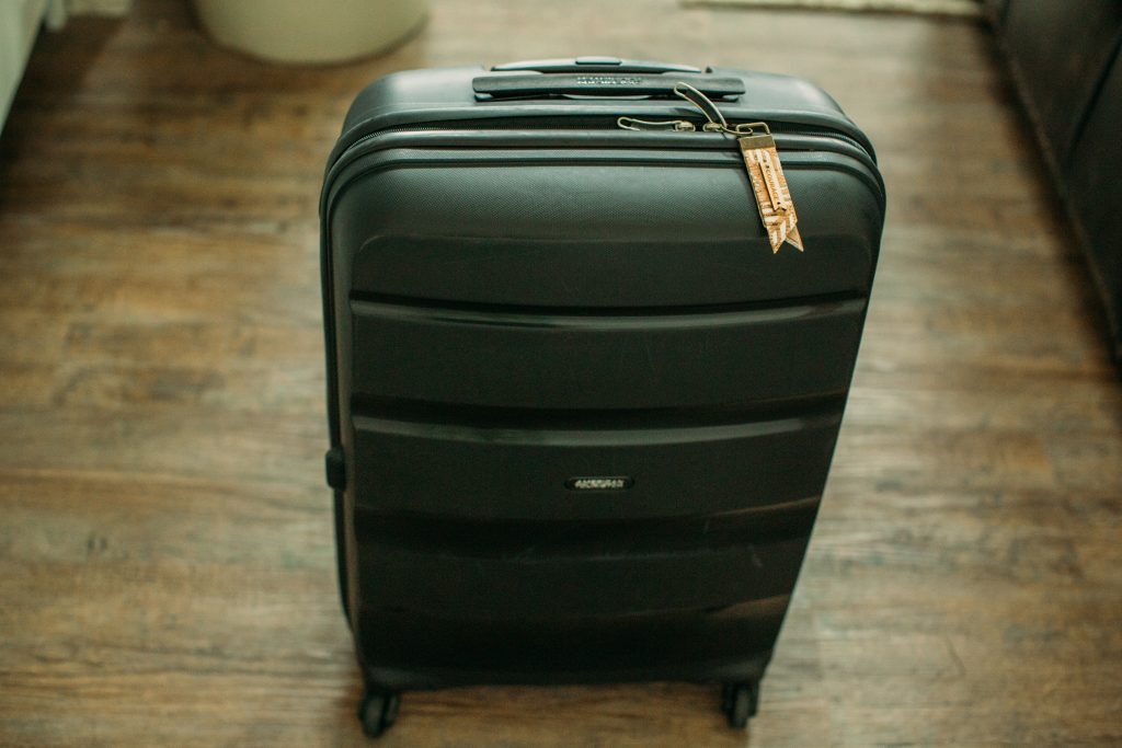 A black rolling shell suitcase with a small luggage tag attached to the handle.