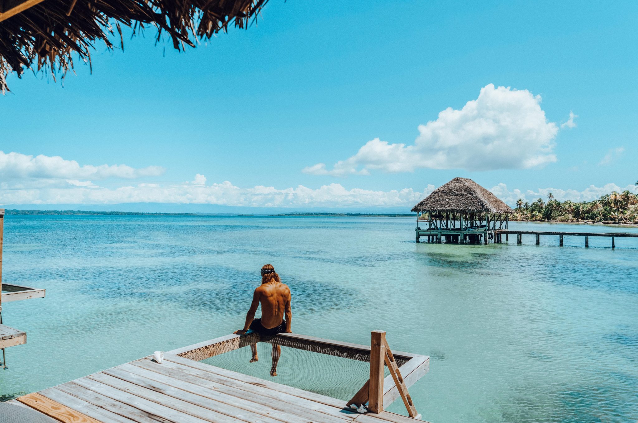 A man sitting on the edge of a dock looking at the ocean and an overwater villa in Azul Paradise, Panama