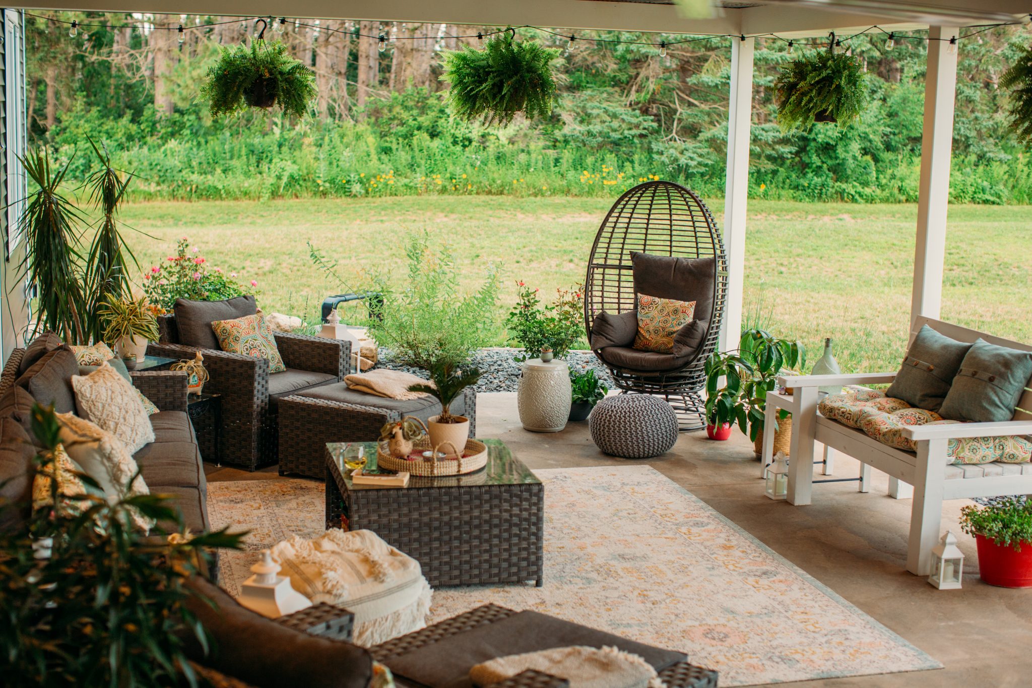 Our cozy backyard patio seating area, complete with a nine-piece outdoor sofa and chair set, a comfortable egg chair, and white bench, all decorated with plenty of pillows and cozy blankets.