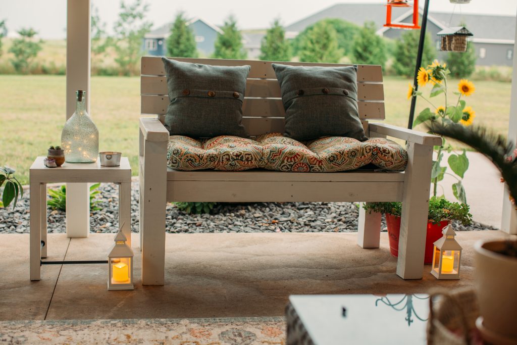 Small lanterns surround the legs of a white wood bench, both filled with citronella candles to keep bugs away from the cozy backyard living space.