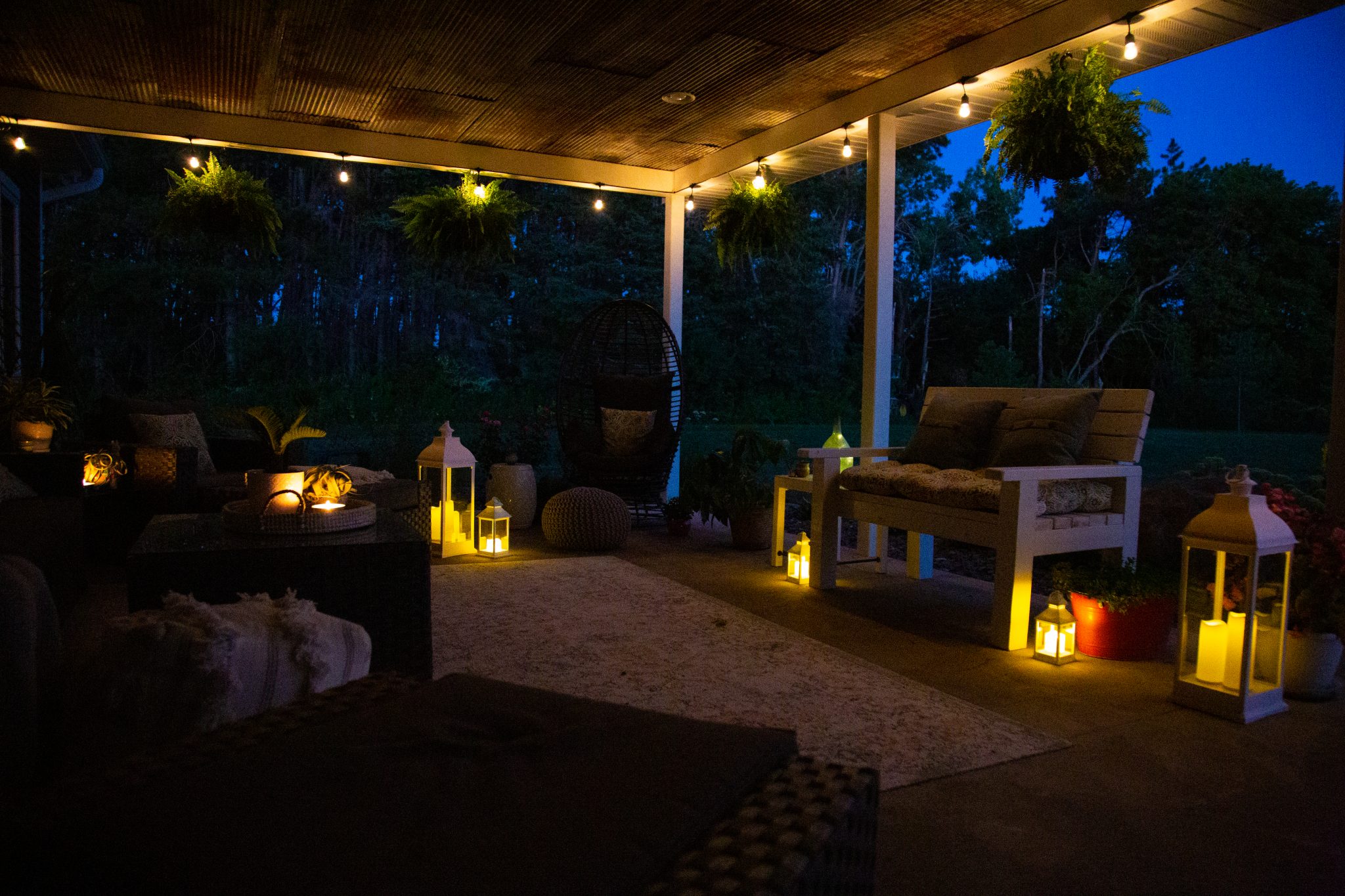 A cozy backyard patio at dusk, softly lit with warm lanterns and string lights around the patio.