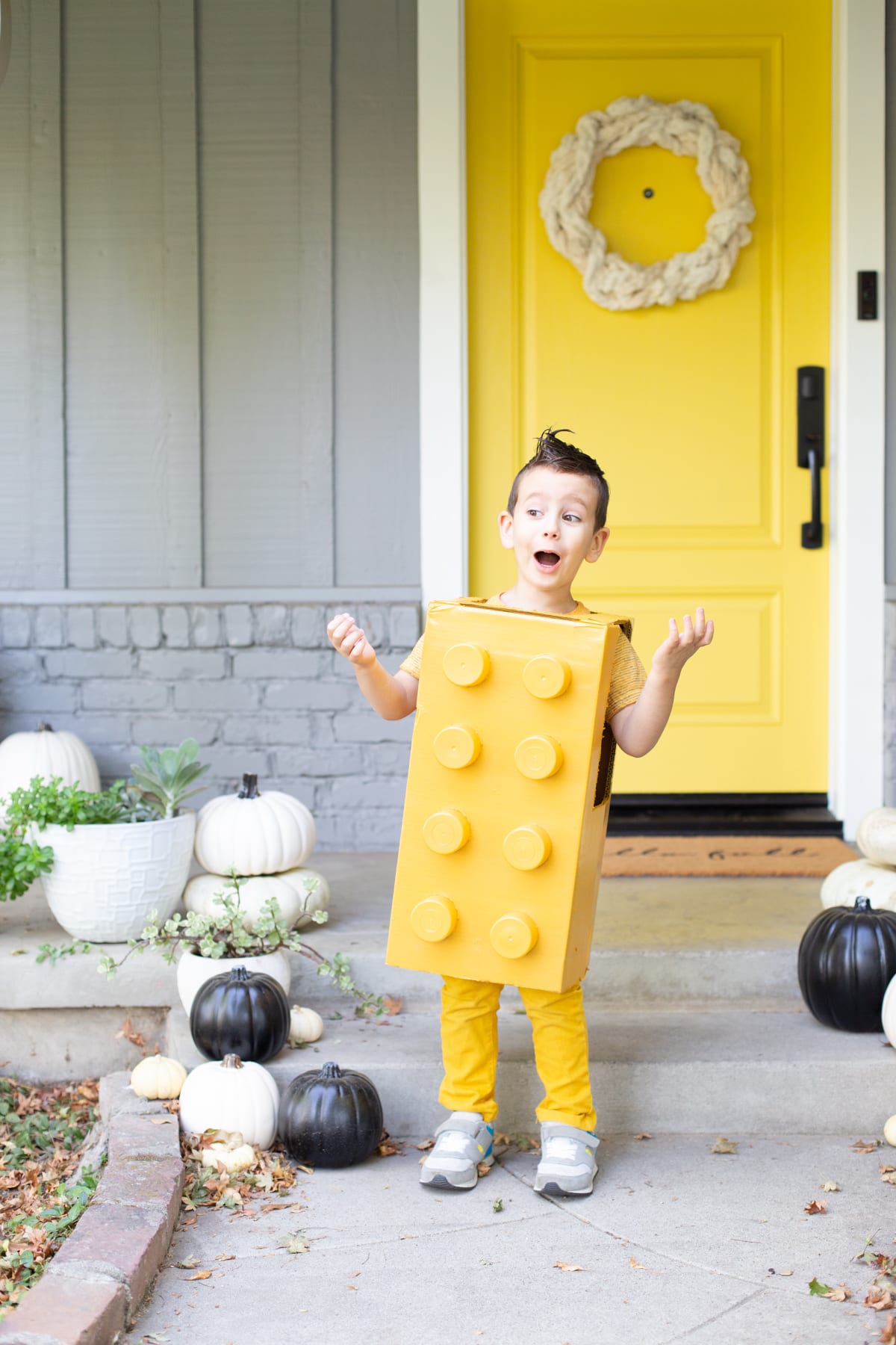 A little boy poses excitedly, wearing a DIY yellow LEGO block costume for trick-or-treating.