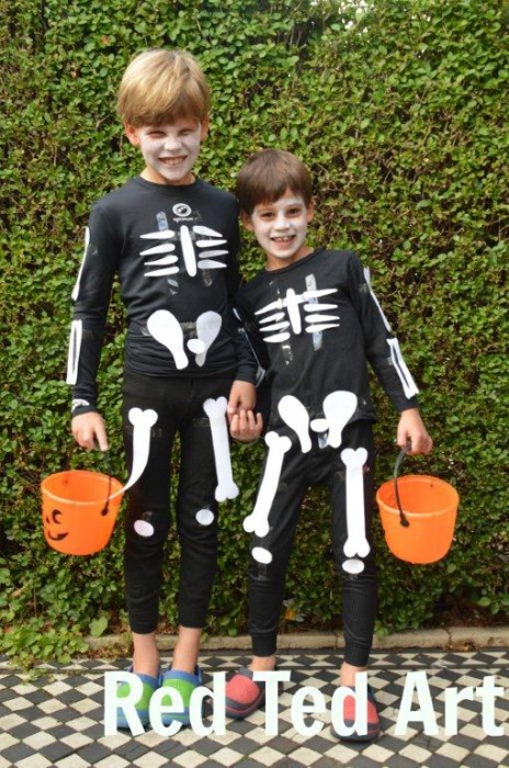 Two young boys are dressed in all black with white bone cutouts attached to their clothes to look like skeletons.