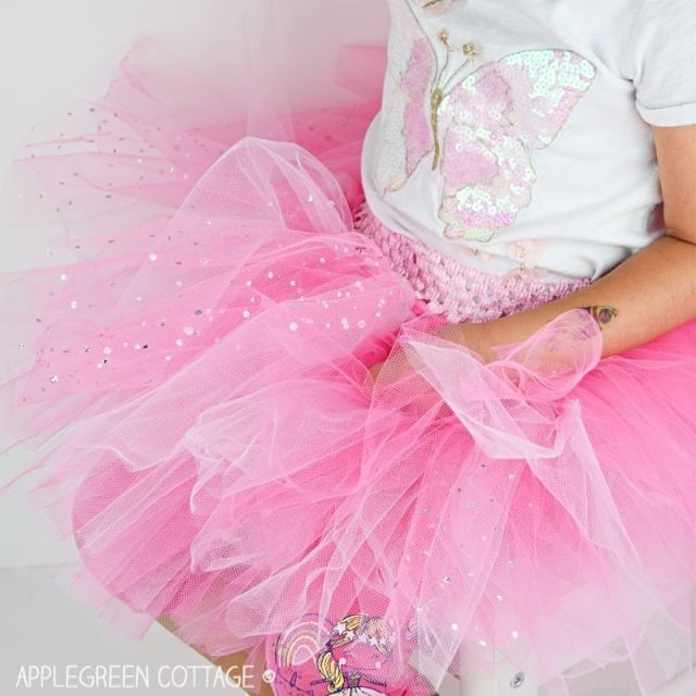 A little girl wears a sparking pink tutu skirt, made with layers of glittery tulle fabric.