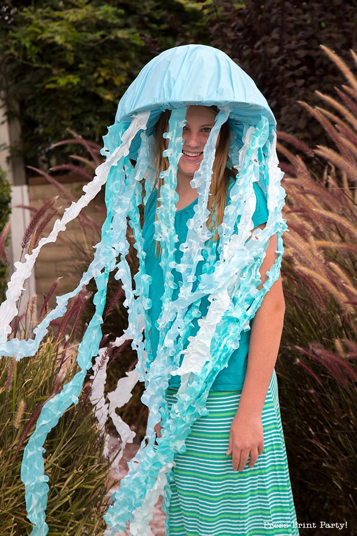 A teenage girl is dressed as a jellyfish, created as a DIY costume. The DIY jellyfish hat has long fabric tentacles hanging down around her body.