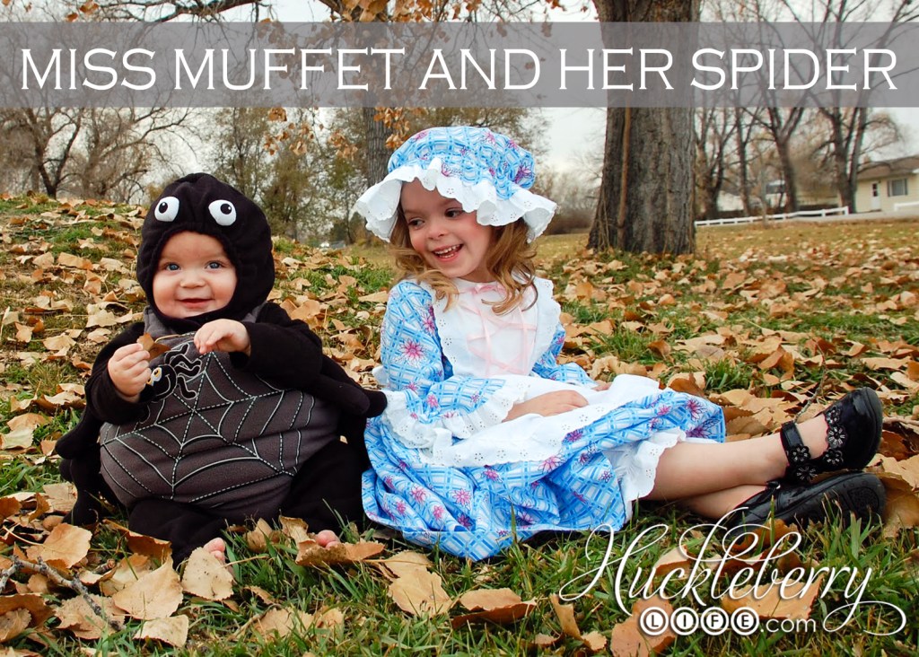 Two children sit on leafy grass in their DIY Halloween costumes. The baby is dressed as a fluffy spider, and the young girl is dressed as Miss Muffet.